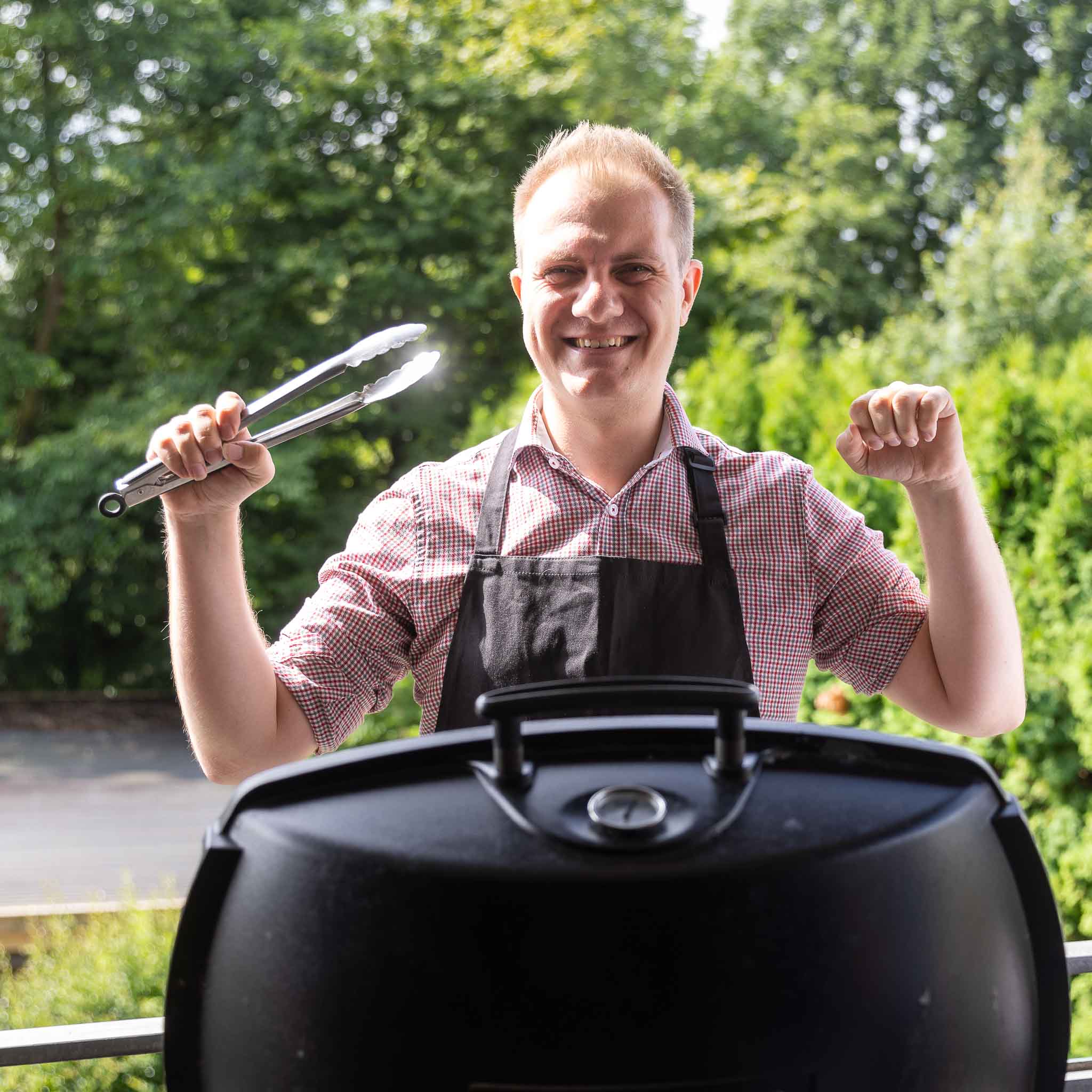 Teammitglied lachend am Grill mit Grillzange